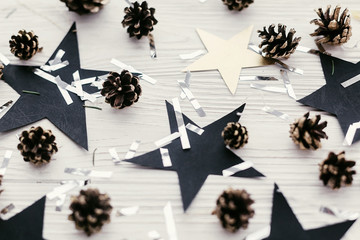 modern christmas image with golden pine cones, silver confetti, black stars on white wood. holiday greeting card. stylish winter flat lay. Merry Christmas