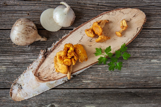 ; Forest mushrooms chanterelle on wooden birch board with white onions. Ingredients for mushroom sauce cooking. Top view, close-up on wooden background