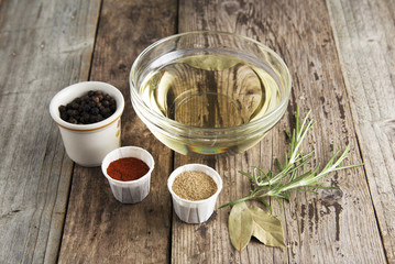 Olive oil and various spices onwooden rustic background: rosemary, paprika, black pepper. Top view.