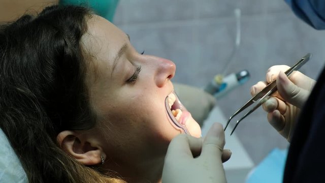 Stomatologist changes the cotton swab in the mouth of the woman, the assistant shines with a dental polymerization ultraviolet lamp on the teeth to the patient. Visit to the dentist