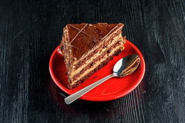 a piece of chocolate cake and cookies with chocolate on a red plate on a dark wooden background. Homemade baking.Close-up view.