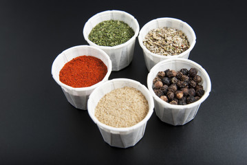 Various spices on black background: rosemary, paprika, black pepper.