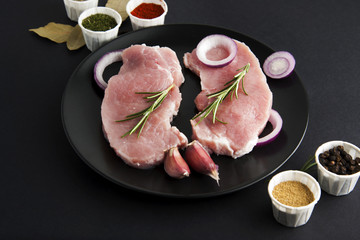 Fresh pork steak, meat with spices for cooking on black background. Food ingredients.