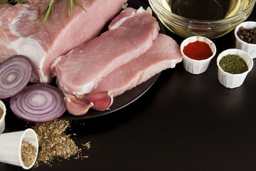 Fresh pork steak, meat with spices for cooking on black background. Food ingredients.