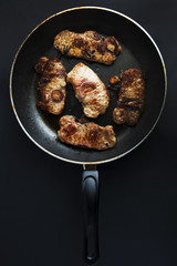 Pork steaks on a frying pan, black background, top view.