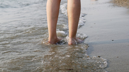 Following a barefoot female feet walking and splashing on sea water waves, cinematic steadicam shot
