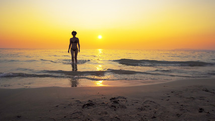 Naklejka premium Sexy fit fashion model go out of sea water with vibrant summer sunset at background