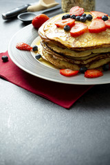 Sweet pancakes with honey, strawberries, and blueberry on a modern white plate. 