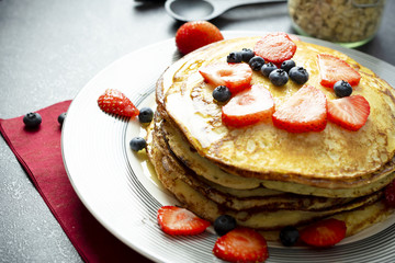 Sweet pancakes with honey, strawberries, and blueberry on a modern white plate. 