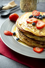 Sweet pancakes with honey, strawberries, and blueberry on a modern white plate. 
