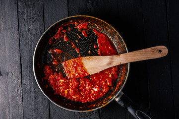 Classic homemade tomato sauce in the pan on a wooden chopping board on brown background, top view....