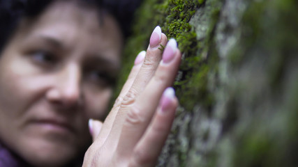 Hugging a nature. A woman puts her arms around large stone with moss, exchanging emotions and charging energy from nature.