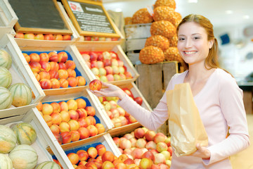 Lady in greengrocers holding paper bag and a nectarine