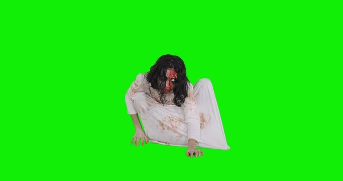 Scary zombie woman with bloody face and white gown, crawling in the studio with green screen background. Shot in 4k resolution