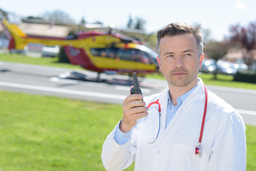 male doctor holding talkie walkie near rescue helicopter