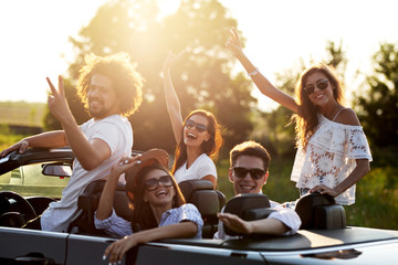 Beautiful stylish  young girls and guys in sunglasses are sitting and laughing  in a black cabriolet on a sunny day.