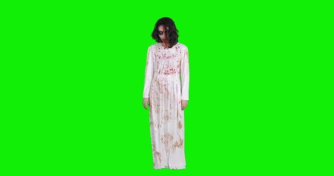 Full length of scary zombie woman with wounded and bloody face standing against green screen background, shot in 4k resolution