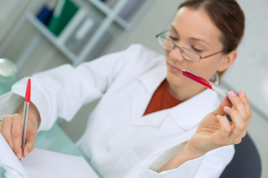 female doctor writing while holding a blood sample