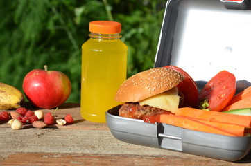 Lunch boxes with food ready to go for work or school, meal preparation or dieting concept. Hamburgers with lettuce. yellow orange juice. with banana nuts. Sliced vegetables carrots and cucumber