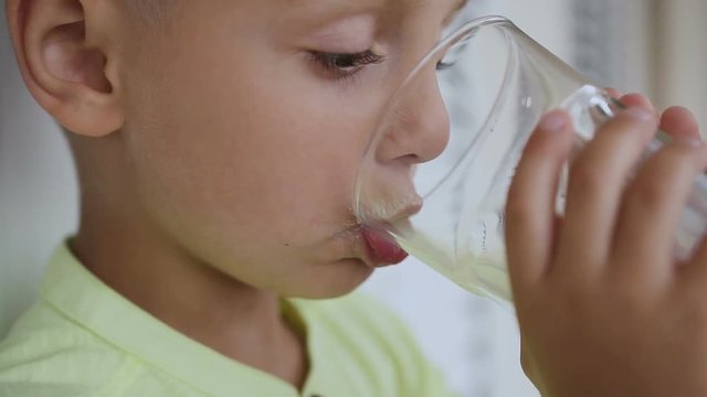 Close-up. Lovely boy is drinking fresh milk and getting milk moustache, isolated on white background. The child drinks a milk drink - kefir, smoothies, cocktail, yogurt.