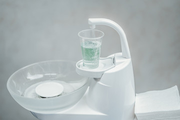 Close up of white dentist spittoon and plastic cup with light green water.