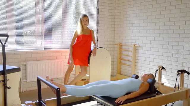 female coach of pilates is talking with client woman during training in a fitness hall