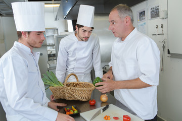 Chef with apprentices teaching about vegetables