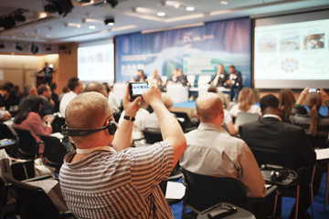Man takes a picture of the presentation at the conference hall using smartphone