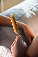 Woman chilling on sofa in daylight and eating ice-cream on stick in sunlight carefree holidays