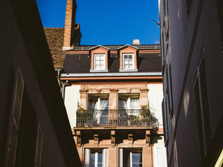 Fototapeta na wymiar From below shot of old beautiful building exterior with balcony and flowers in sunlight in cute Parisian French building 