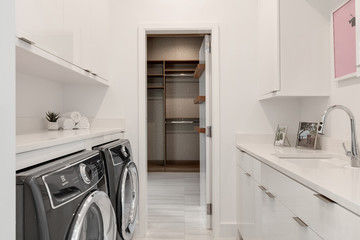 modern white laundry room with sink, washer, dryer looking into walk in wardrobe