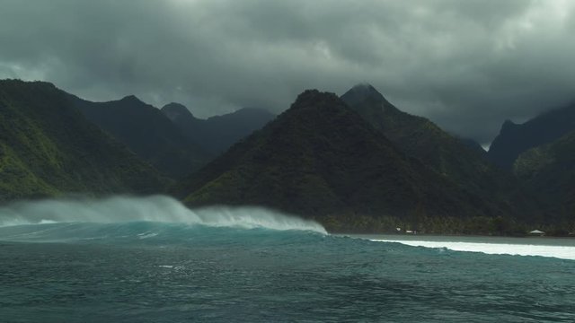 SLOW MOTION: Dark clouds gather over the lush exotic island in the Pacific right before a violent rainstorm. Big turquoise colored breaking waves crash towards the exotic island in French Polynesia.