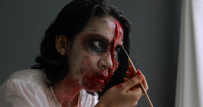 Young woman applying scary halloween makeup on her face with a brush. Shot in 4k resolution