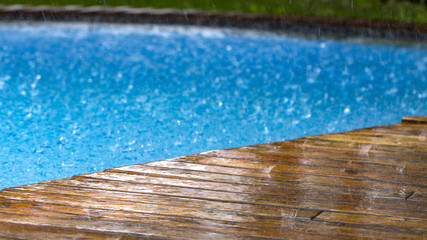 drops of rain fall on a wooden terrace and a bridge near the pool