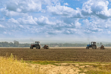 Obraz premium Beautiful agricultural landscape under the cloudy sky - two old tractors equipped with seeders. Farmers sowing winter wheat in autumn