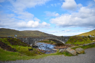 Fototapeta na wymiar Old vintage brick bridge crossing river in Sligachan. Isle of Skye, Highland, Scotland, United Kingdom, August, 2018