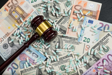 Wood judge's gavel and scattered colorful drugs on the dollar and euro cash background