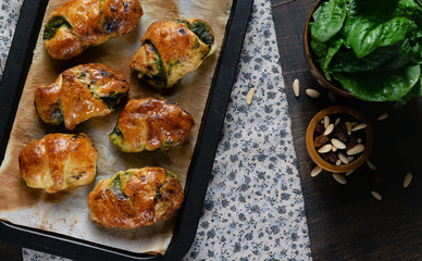 Homemade recipe of croissants stuffed with spinach and ricotta on baking paper in baking dish. Dark rustic background. Banner. Top View. Copy space Healthy recipe concept.