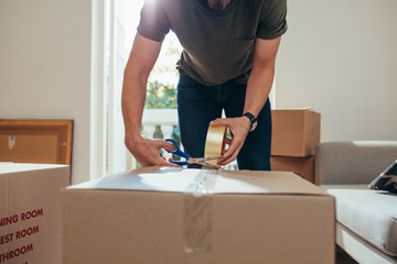 Man packing his household stuff in packing boxes and sealing the