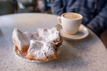 Obraz na płótnie Canvas Beignets covered with powdered sugar, served with cafe au lait at the famous Cafe Du Monde in the French Quarter. Shallow focus on the powdered sugar for effect.