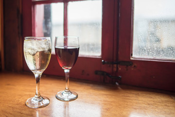 Glasses of wine, red and white, in front of a window on a train, ready to drink and comforting, with a rainy day outside.