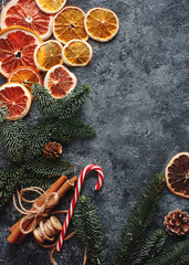 Christmas or New Year flat lay home decor, dry oranges, cinnamon, candies and fir branches on concrete background. Cozy winter homely scene, top view, copy space