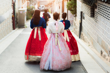 Naklejka premium Tył trzech kobiet w hanbokach spacerujących po tradycyjnych domach w wiosce Bukchon Hanok w Seulu w Korei Południowej.