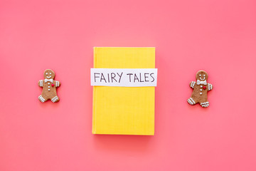 Fairy tales book near gingerbread man on pink background top view copy space