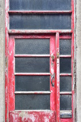 Fototapeta na wymiar Weathered wooden door painted red with metal handle and brass lock. Window panes have wire mesh for protection.