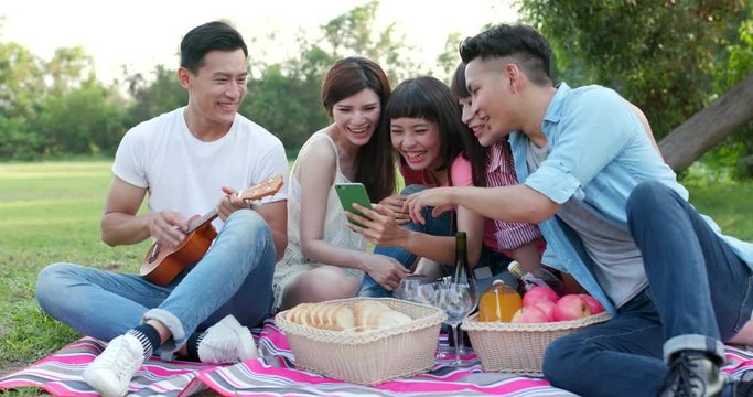 Friends go picnic together and share happiness on cellphone