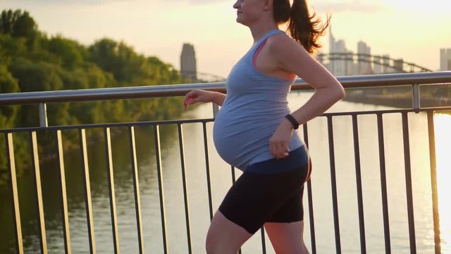 Active pregnant woman running across the bridge with a beautiful view of the city of Frankfurt in Germany