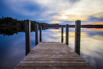 Summer Sunset Lake.. Sunset reflected in the blue water of Brevort Lake with wooden dock in the foreground. Brevort Lake is part of the Hiawatha National Forest of Michigan.