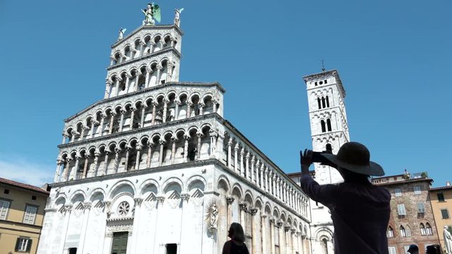 Woman's silhouette with straw hat taking picture of San Michele in Foro, Lucca. Female traveler visiting church of St. Michael, tourist walking in front of roman cathedral landmark of Tuscany, Italy