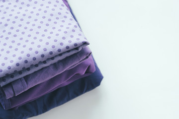 Different cloth in violet color stack on a white table with copy space.